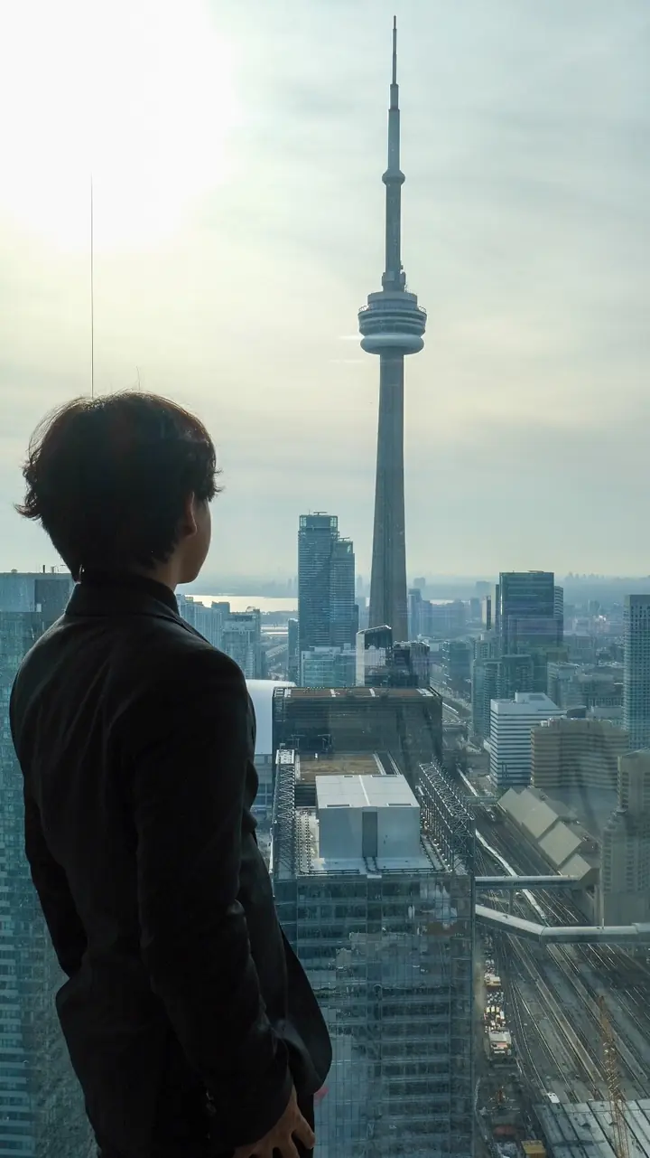 A student in a dark blazer, seen from behind, looking out over the CN Tower from high in the building at UEC 2025.